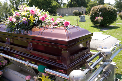 Picture of a coffin at a cemetery with flowers on top of it