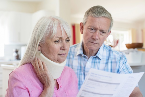 Woman in a neck cast at the hospital reading her bill with her husband at her side