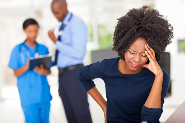 Woman at the hospital holding her back and her head in pain after a car wreck with two doctors in the background